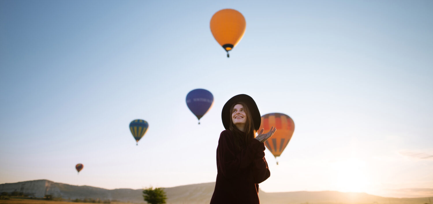 A woman watches hot air balloons in the sky.